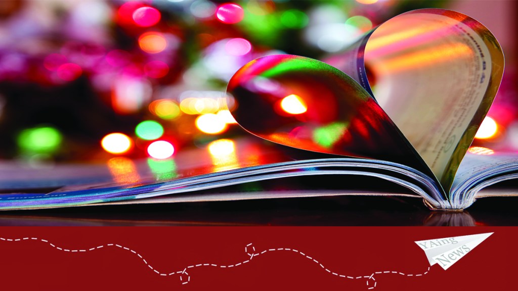 Book pages folded in the shape of a heart, with Christmas lights shining in the background.