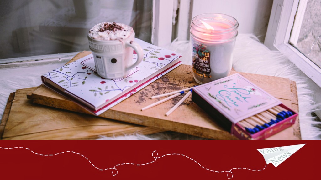 The YAing News paper airplane under an image of a winter candle, a mug of hot chocolate, and a box of matches.