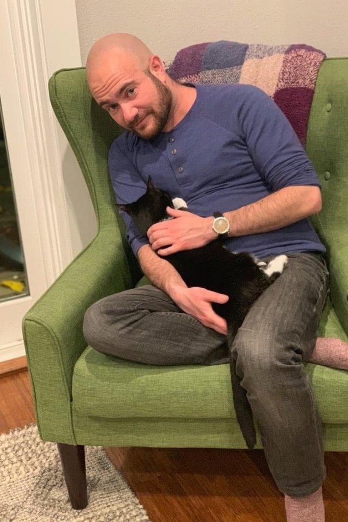 Author Kyle Lukoff sits and holds a cat.